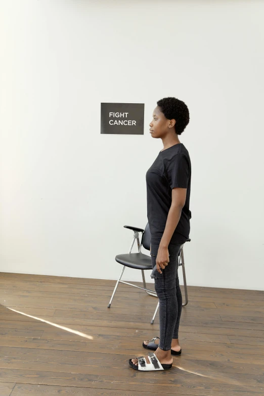 a woman standing in front of a wall with a sign on it, by Marina Abramović, visual art, sitting on chair, physically accurate, physicality-based render, fight