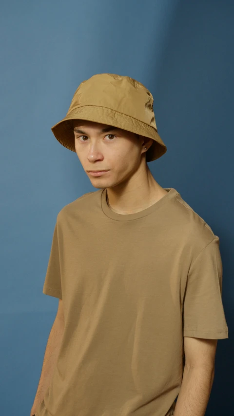 a young man standing in front of a blue wall, inspired by Junpei Satoh, instagram, bucket hat, light brown, 8k octan photo