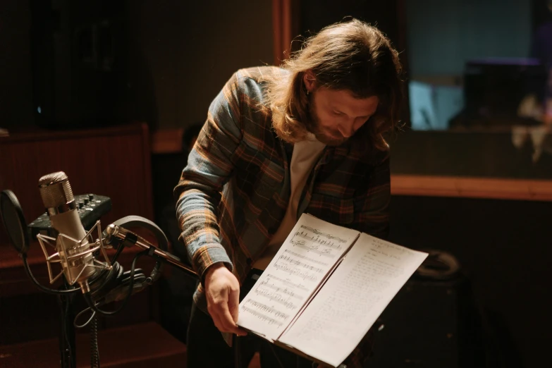 a man holding a sheet of paper in front of a microphone, an album cover, unsplash, crewdson, sheet music, studio recording, charlie day