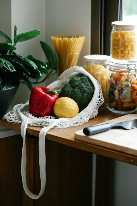 a table topped with lots of food next to a window, a still life, pexels, jar on a shelf, pasta, veggies, cloth accessories