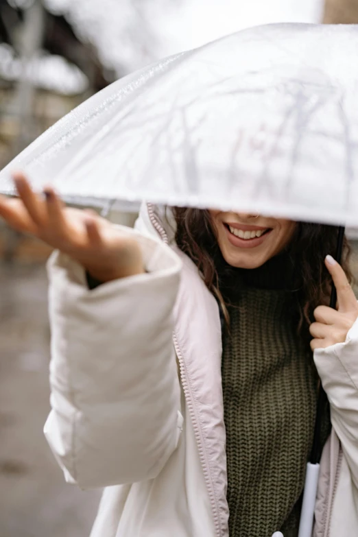 a woman holding an umbrella over her head, a picture, trending on unsplash, a still of a happy, winking, moisture, grey