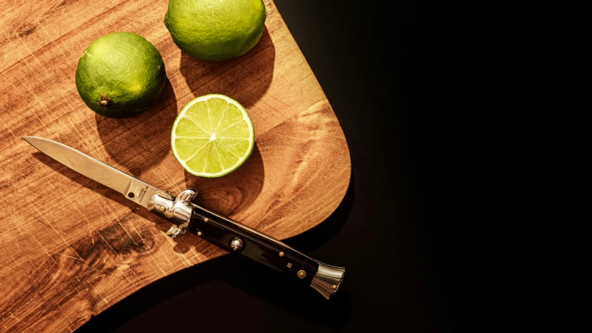 a cutting board with limes and a knife on it, a still life, by Matthias Stom, trending on pexels, in style of chrome hearts, 🍸🍋, close up high detailed, miniature product photo