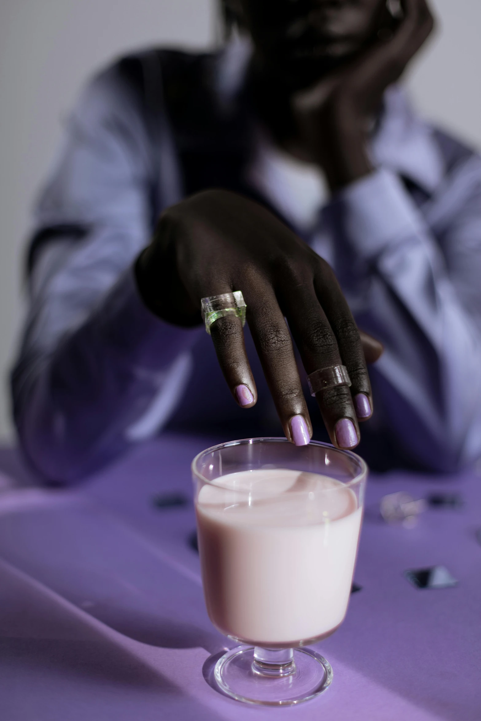 a woman sitting at a table with a glass of milk, an album cover, trending on unsplash, hyperrealism, purple skin color, holding hand, black skin, extremely pale