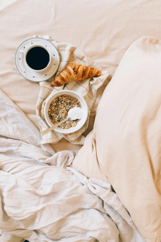 a person laying in bed with a cup of coffee and croissants, trending on unsplash, cereal, gold linens, beige, black
