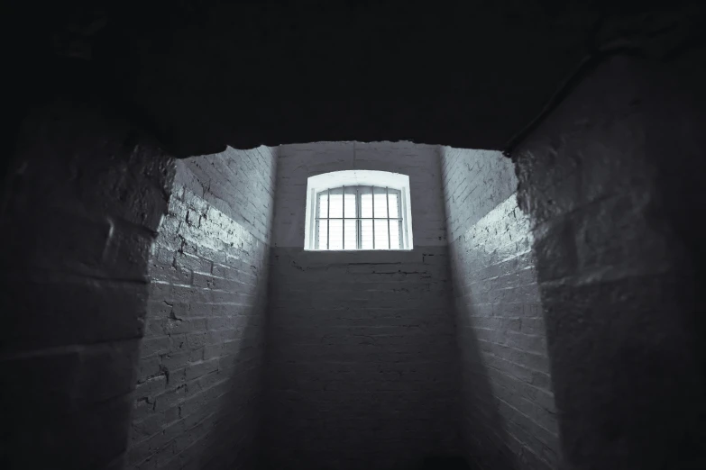 a black and white photo of a window in a brick wall, pexels contest winner, light and space, in a small prison cell, dimly lit underground dungeon, instagram post, colour photograph