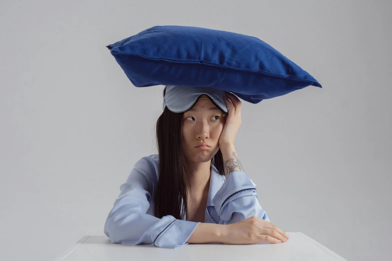 a woman sitting at a table with a pillow on her head, an album cover, inspired by Fei Danxu, ultramarine, taken with sony alpha 9, gongbi, frown fashion model