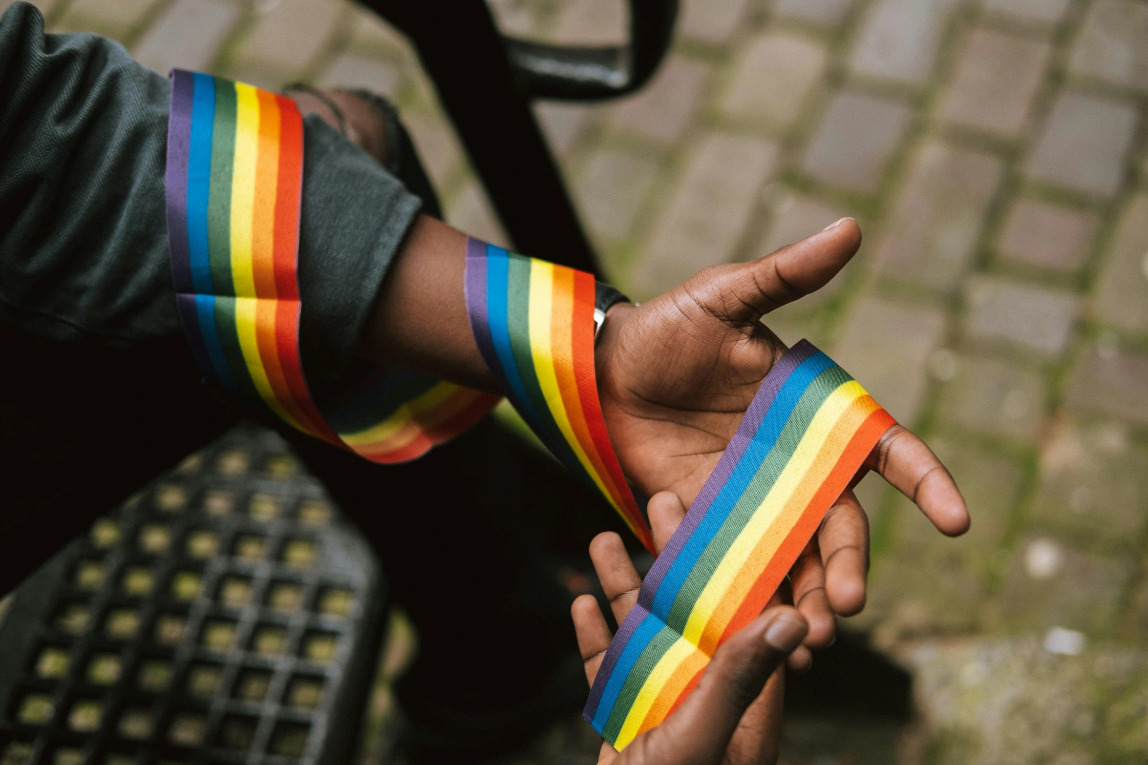 a close up of a person holding a rainbow ribbon, by Nina Hamnett, trending on pexels, bandage taped fists, riyahd cassiem, exterior shot, gauntlets