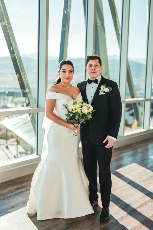 a man in a tuxedo standing next to a woman in a wedding dress, skybridge towers, with backdrop of natural light, pablo carpio and jordan grimmer, mountain in background