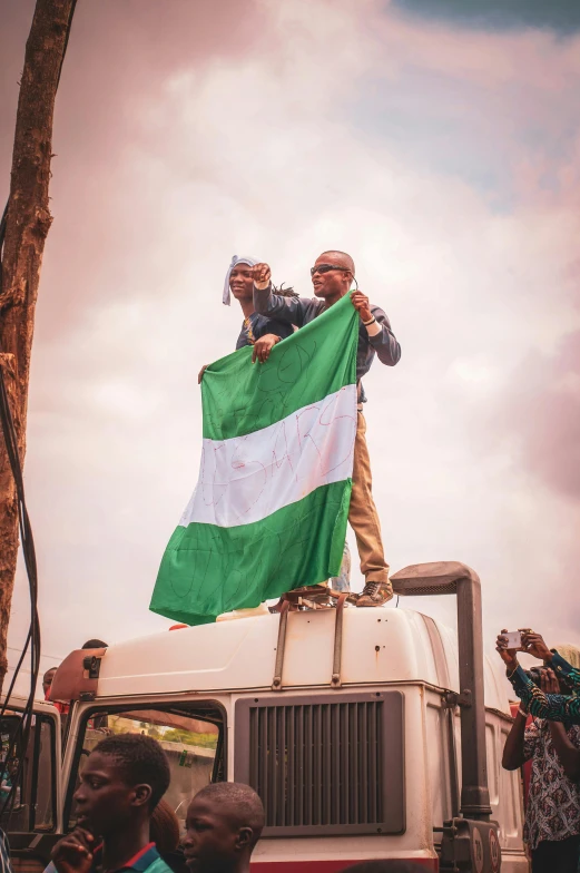 a group of people standing on top of a truck, by Matija Jama, trending on unsplash, happening, green flags, kano), holding a white flag, adebanji alade