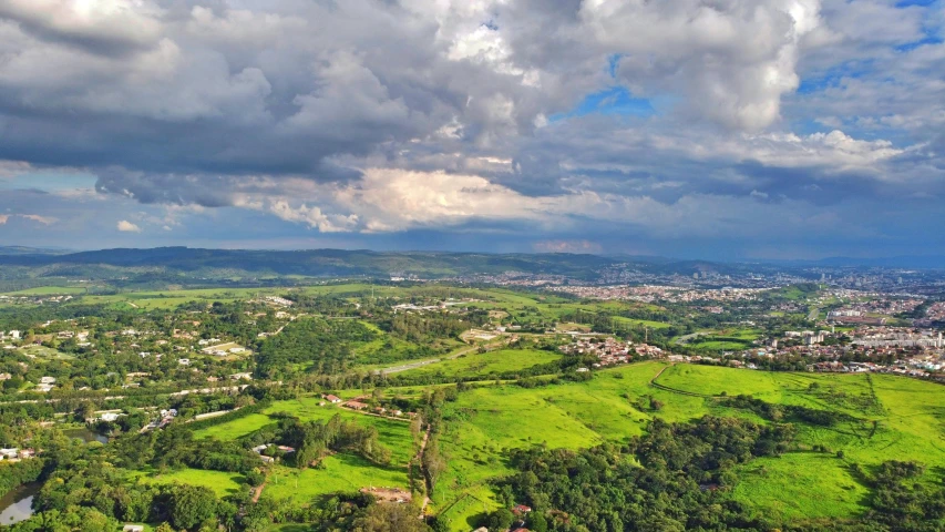 a view of a city from the top of a hill, city of armenia quindio, verdant green fields, oscar niemeyer, rain lit