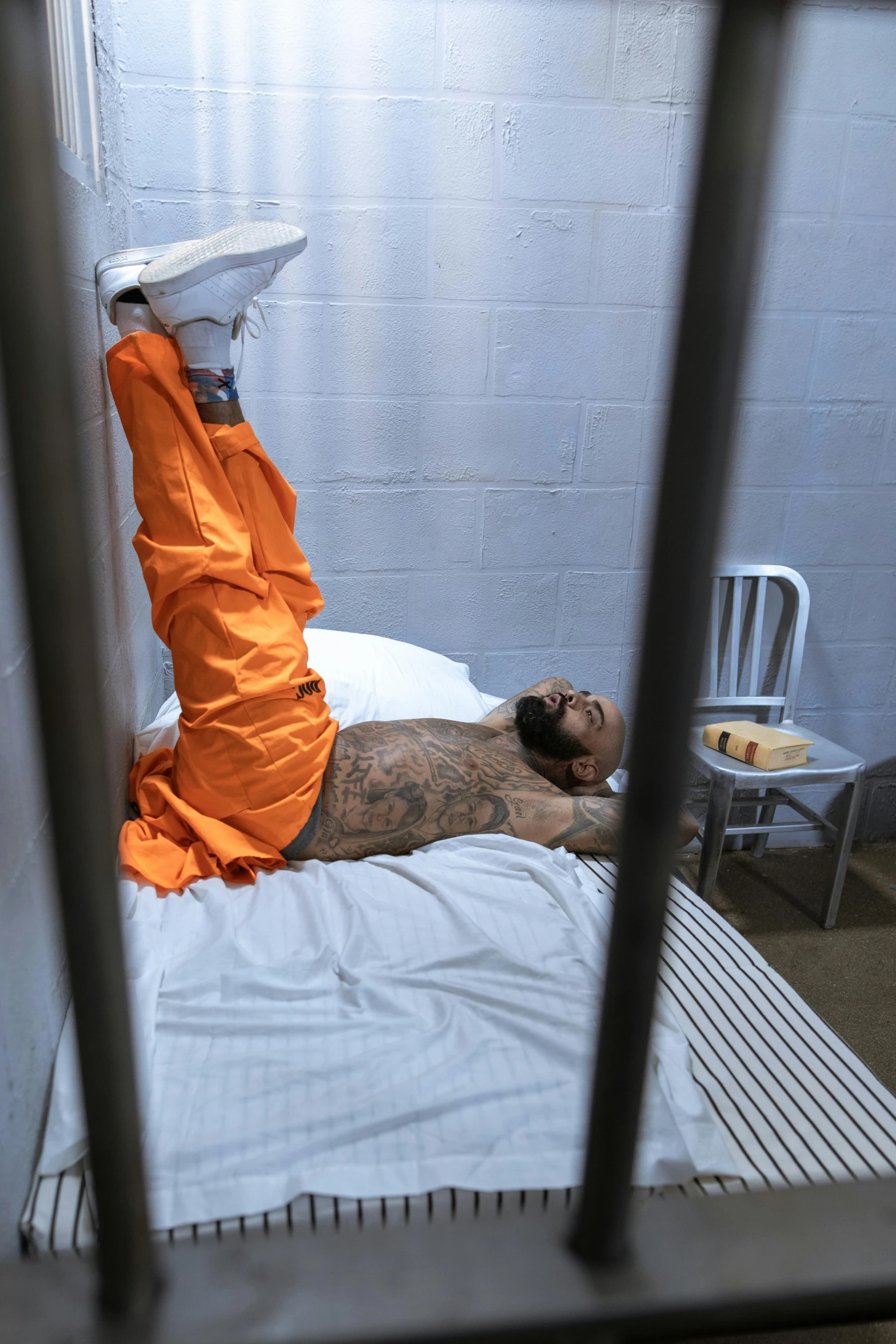 a man laying on top of a bed in a jail cell, a tattoo, happening, orange gi, 2019 trending photo, ap, he is a long boi ”