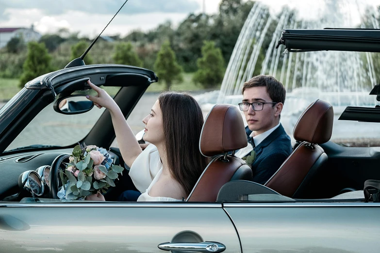 a man and a woman in a convertible car, by Matt Cavotta, unsplash, formal wear, overlooking, floating bouquets, “ iron bark