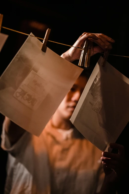 a person hanging pictures on a clothes line, an album cover, pexels contest winner, theatrical lighting, bags, collodion photography, detail shot