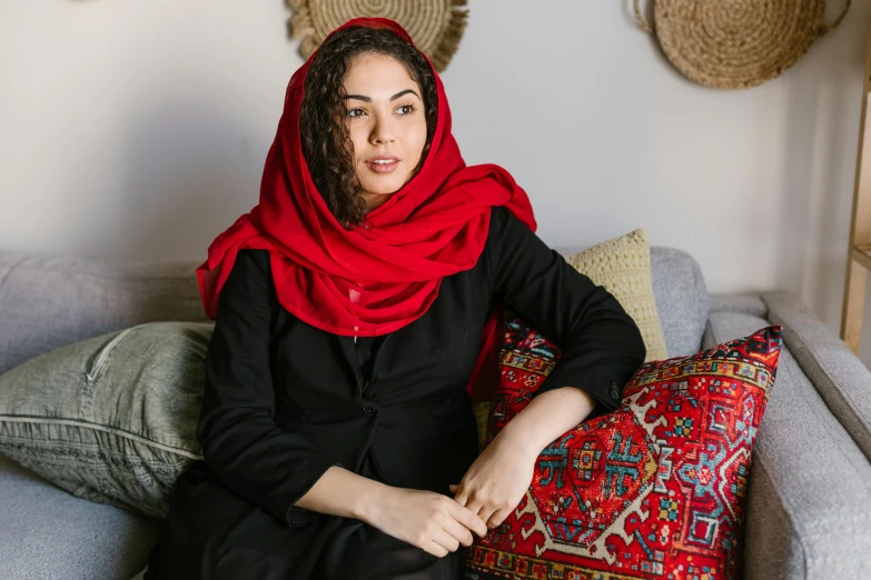 a woman sitting on a couch wearing a red scarf, inspired by Maryam Hashemi, pexels contest winner, seated in royal ease, black, iranian, casually dressed