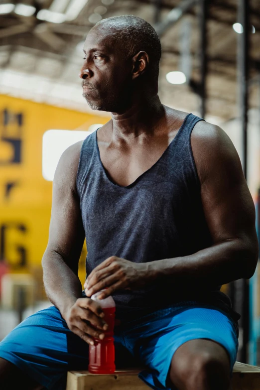 a man sitting on a bench in a gym, pexels contest winner, happening, man is with black skin, holding a bottle, profile image, serious