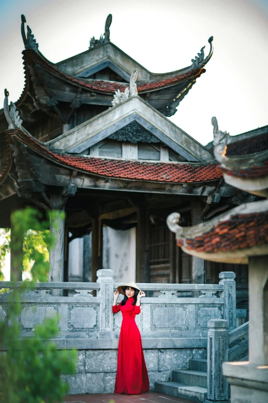 a woman in a red dress standing in front of a building, inspired by Cui Bai, red roofs, vietnam, temple, taking a picture