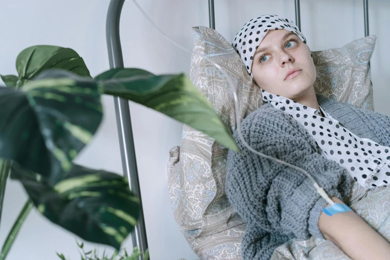 a woman laying in a bed next to a plant, trending on pexels, hurufiyya, wearing a head scarf, injured, sophia lillis, tumours