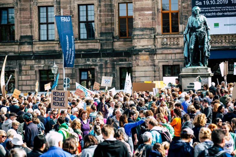 a crowd of people standing in front of a statue, by Matija Jama, pexels, happening, placards, climate change, blue text that says 3kliksphilp, royal photo