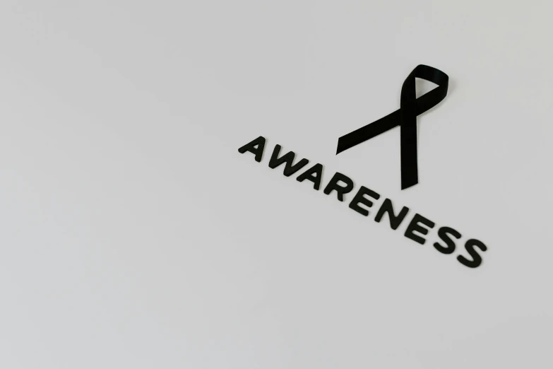 a black ribbon with the word awareness on it, a picture, pixabay, negative space is mandatory, on grey background, background image, on a black wall