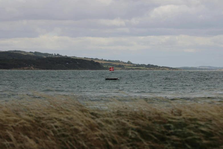 a body of water with a boat in the middle of it, a picture, windy day, view from a distance, lachlan bailey, slightly red