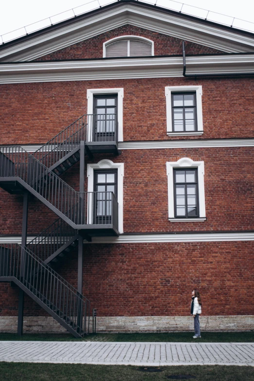 a person standing in front of a red brick building, inspired by Mihály Munkácsy, pexels contest winner, external staircases, finland, low quality photo, high resolution photo