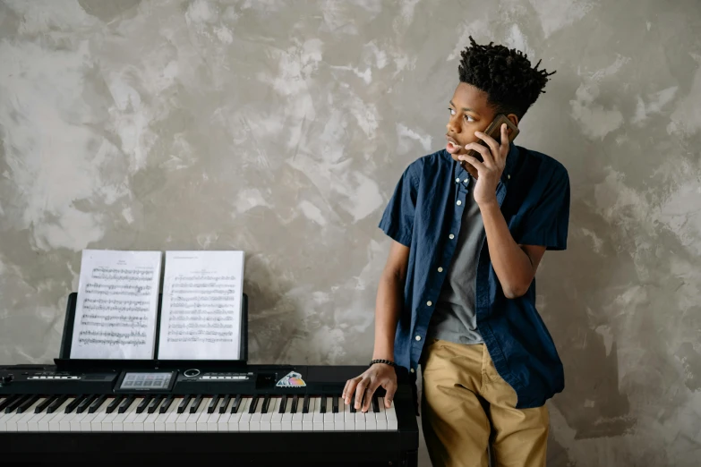 a young man talking on a cell phone next to a piano, trending on pexels, ashteroth, aged 13, professional modeling, music instrument in hand