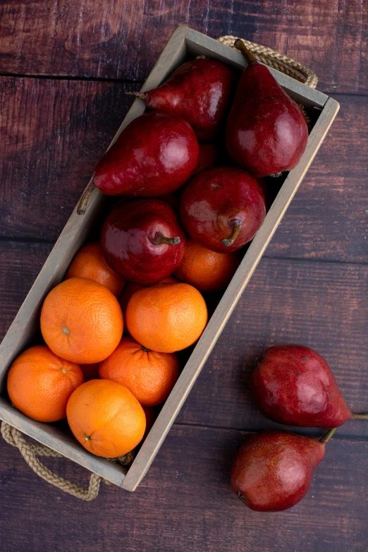 a box of fruit sitting on top of a wooden table, red and orange colored, uncropped, square, long