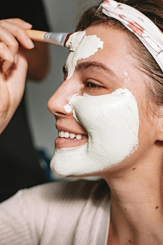 a woman is putting a mask on her face, her face is coated in a whitish, ultra texture, smiling mask, sculpted