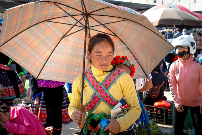 a woman holding an umbrella in a crowded market, a portrait, inspired by Cui Bai, pexels contest winner, square, tribal clothing, avatar image, slightly sunny