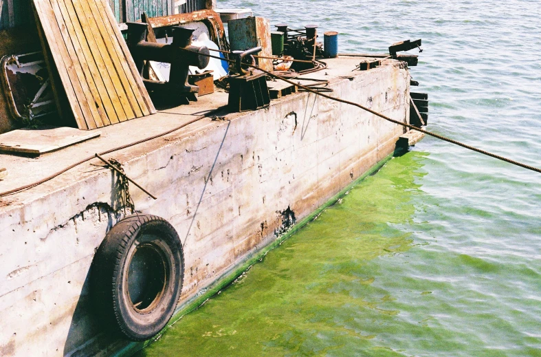 a boat that is sitting in the water, an album cover, unsplash, hurufiyya, rusty vehicles, algae feet, 2 0 0 2 photo, construction