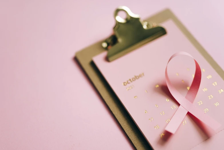 a clipboard with a pink ribbon on it, by Julia Pishtar, pexels contest winner, happening, pink and gold, female calendar, october, thumbnail