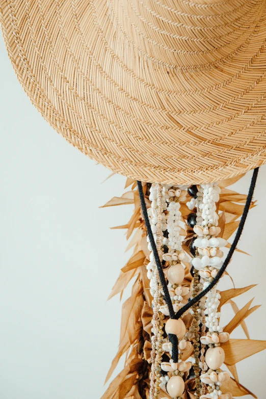 a straw hat sitting on top of a wooden table, strings of pearls, in a white boho style studio, maximalist details, neck zoomed in