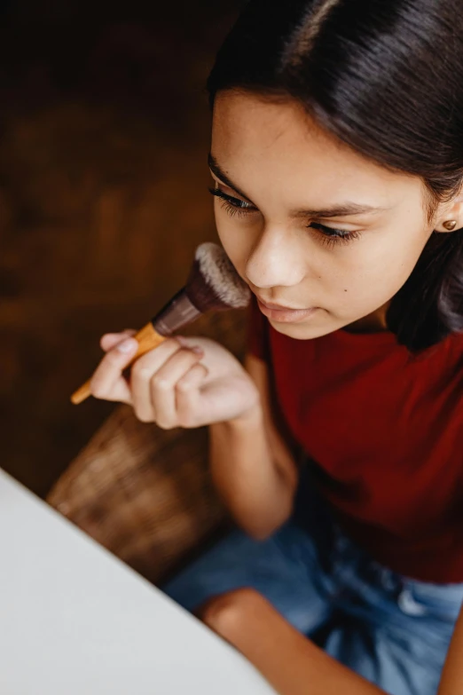 a woman sitting at a table eating a piece of food, an airbrush painting, pexels contest winner, village girl reading a book, holding paintbrushes, cinnamon skin color, with a pointed chin