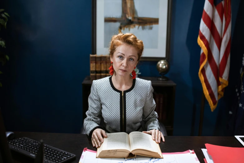 a woman sitting at a desk with an open book, a portrait, inspired by Nil Gleyen, pexels, photorealism, still from better call saul, president of belorussia, in style of nan goldin, holding court