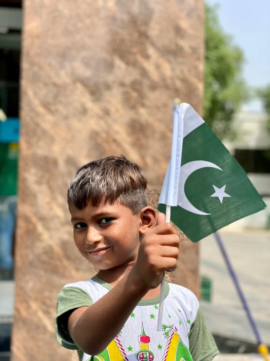 a young boy holding a pakistan flag in front of a building, pexels contest winner, 15081959 21121991 01012000 4k, big smirk, high angle close up shot, high-quality photo