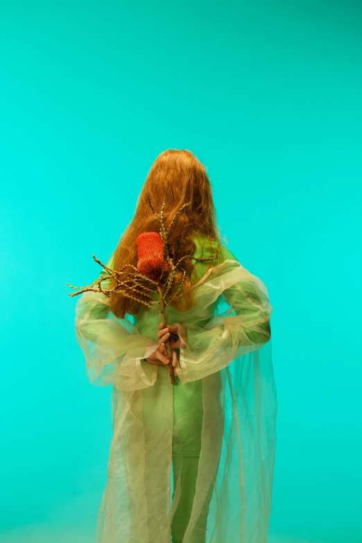 a woman in a green dress holding a flower, an album cover, inspired by Elsa Bleda, long orange hair floating on air, dressed in plastic bags, porcelain holly herndon statue, rear-shot