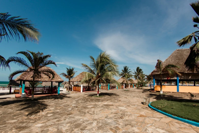 a sandy beach with thatched huts and palm trees, an album cover, trending on unsplash, happening, village square, somalia, walkway, on a bright day