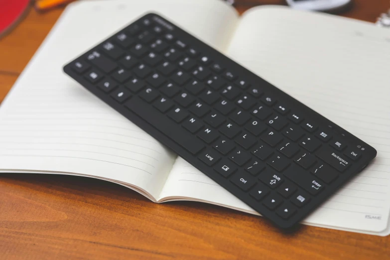 a black keyboard sitting on top of an open book, on a table, neoprene, handheld, commercially ready