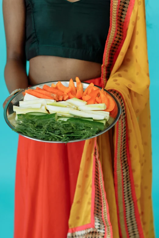 a woman holding a tray of carrots and veggies, inspired by Nam Gye-u, wearing bihu dress mekhela sador, medium detail, hand on hips, chartreuse and orange and cyan