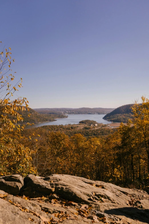 a man sitting on top of a rock next to a lake, a picture, unsplash, hudson river school, panorama distant view, during autumn, looking over west virginia, slide show