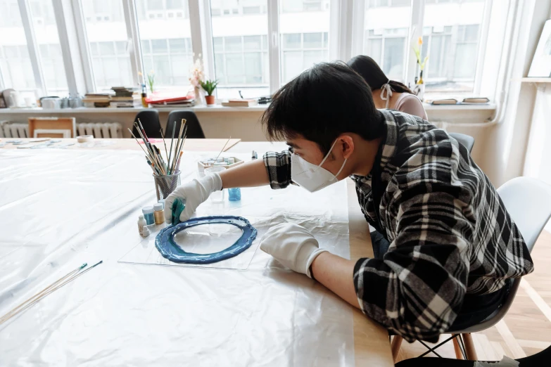 a person sitting at a table working on something, inspired by Fei Danxu, pexels contest winner, arbeitsrat für kunst, wearing facemask, resin painting, school class, studio shot