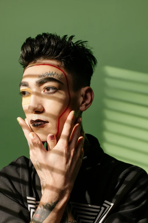 a man standing in front of a green wall, an album cover, inspired by Taro Yamamoto, trending on pexels, elaborate patterned makeup, attractive androgynous humanoid, realistic. cheng yi, square masculine jaw