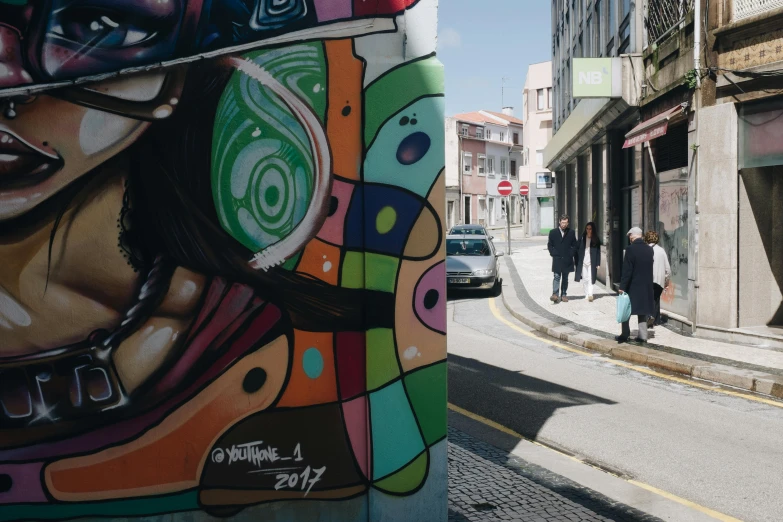 a painting on the side of a building next to a street, graffiti art, by Okuda Gensō, pexels contest winner, the city of lisbon, people walking around, medium shot taken from behind, shot on sony a 7 iii