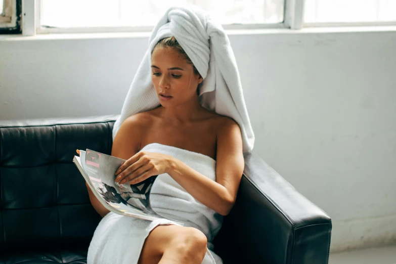 a woman in a towel sitting on a couch reading a magazine, a portrait, pexels contest winner, private press, sleek robes, wet hair, skincare, slightly tanned