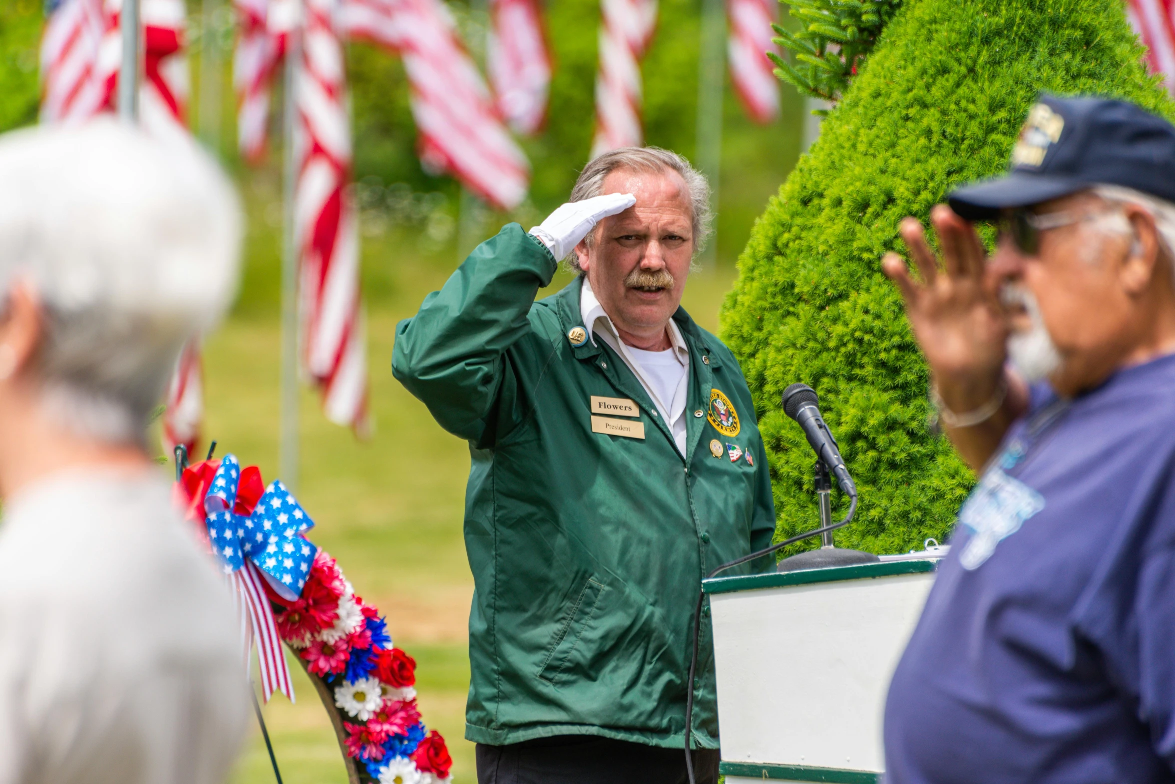 a man that is standing in front of a microphone, green flags, american veteran gi, flowers around, profile image