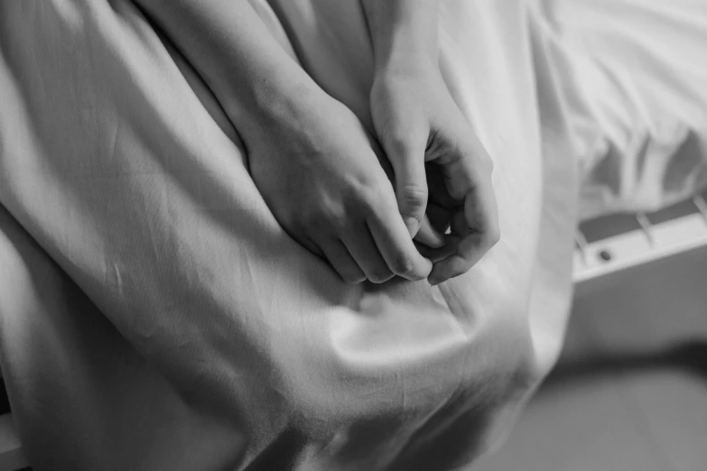 a black and white photo of a person sitting on a bed, by Emma Andijewska, pexels, figuration libre, unclipped fingernails, wearing white silk, hurting, actual photo