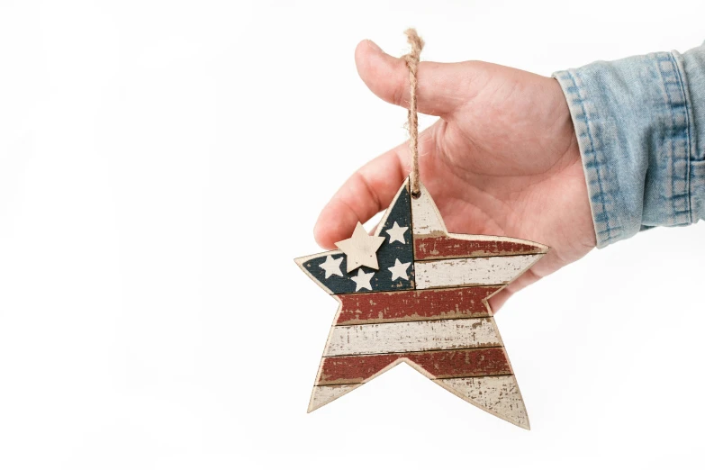 a person holding a wooden star ornament, by Joe Bowler, pexels, american flag, set against a white background, made of glazed, retro vibe