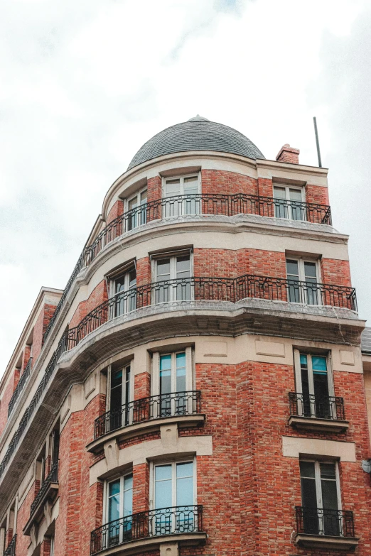 a tall red brick building sitting on the side of a street, a photo, trending on unsplash, paris school, rounded roof, balcony, high-resolution photo, multiple stories