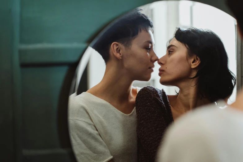 a man and woman kissing in front of a mirror, trending on pexels, hyperrealism, lesbian, looking towards the camera, two women, embracing