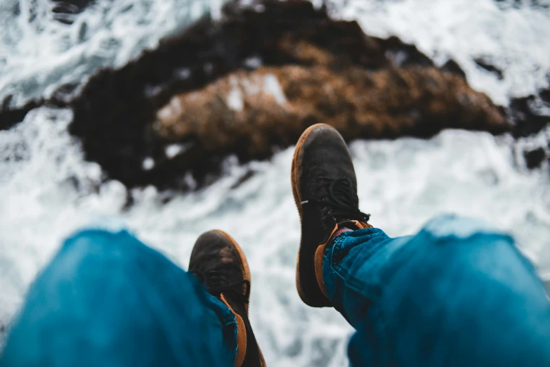 a person standing on top of a rock next to the ocean, trending on pexels, happening, brown boots, looking up at the camera, sitting down casually, close up shot from the top